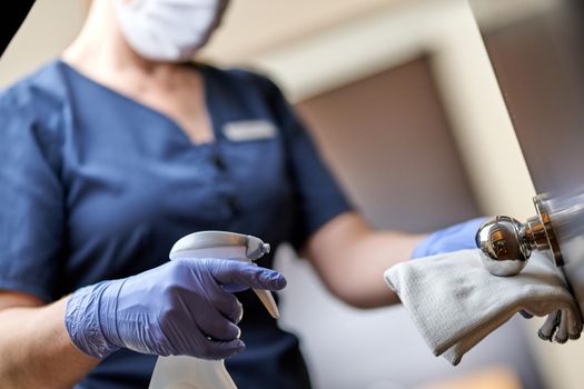 Cropped photo of chambermaid wearing gloves and wiping the door handle with a special disinfectant. Hotel service concept