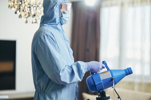 Side view of worker in protective overalls making disinfection to prevent the spread of covid19 in hotel room. Coronavirus and quarantine concept