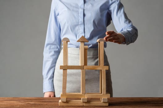 Business woman building tower on table from wooden blocks. Strategy planning and development concept. Young woman wearing formal wear sitting in office interior. Successful company building and growth