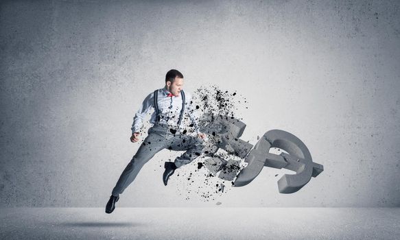 Young furious businessman jumping and crashing with kick stone dollar symbol