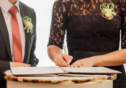 The hand of the girl witness the bride and groom at the wedding puts the signature pen.
