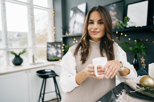 Attractive young woman drinks tea in the kitchen for Christmas day