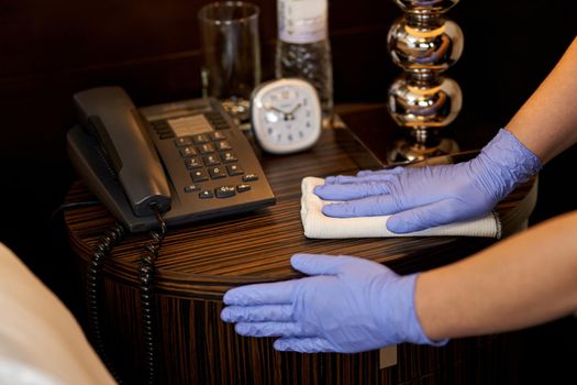 Cropped photo of maid wearing protective gloves and wiping furniture with a rag. Hotel service concept