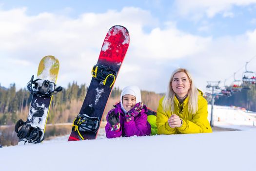 Mother and daughter with snowboards are playing in the snow