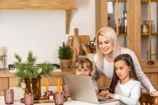Happy loving family. Young mother and daughters girls using laptop. Funny mom and lovely children are having fun staying at home.
