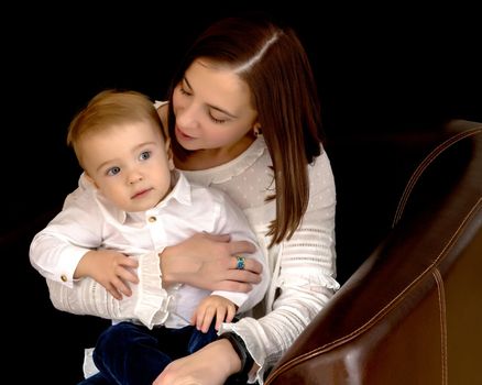 Young mother with a small son in her arms on a black background. The concept of a happy childhood, advertising.