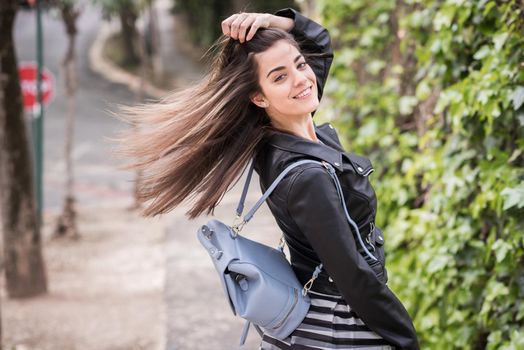 Young woman moving her hair in urban background wearing leather jacket