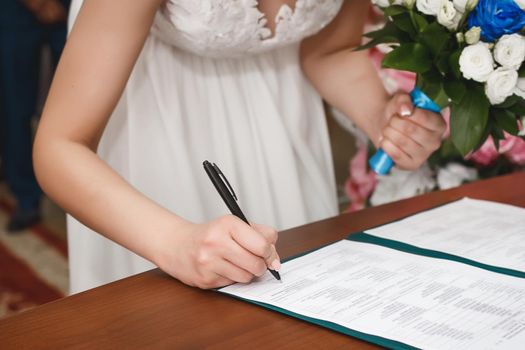 The hand of a young girl bride at the wedding puts the signature of consent to marriage in the document in the registry office.