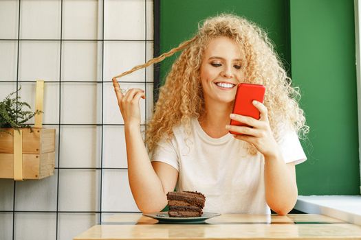 Attractive blonde woman sitting near window in cafe and using her mobile phone