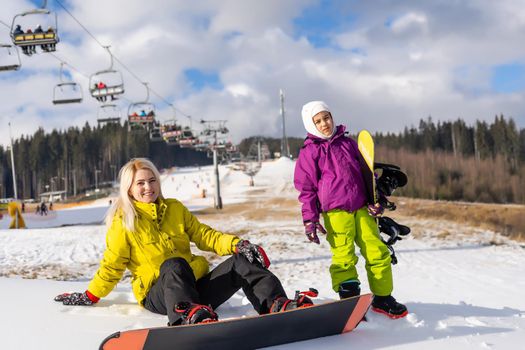 Mother and daughter with snowboards are playing in the snow