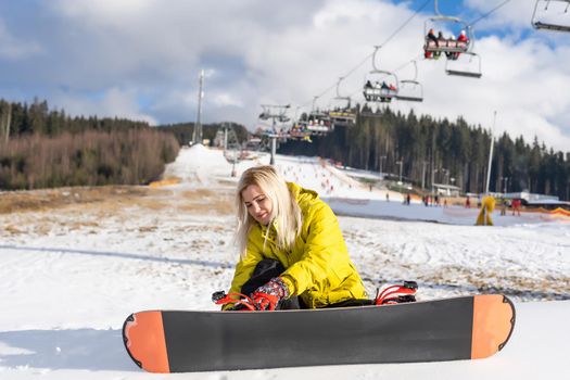 Young woman with snowboard sitting on the slope of hill