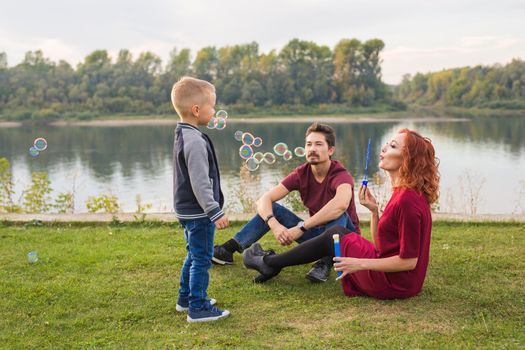 People and nature concept - Mother, father and their child playing with colorful soap bubbles.