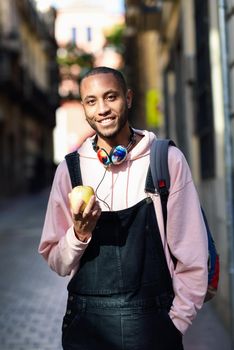 Young black man eating an apple walking down the street. Lifestyle concept.