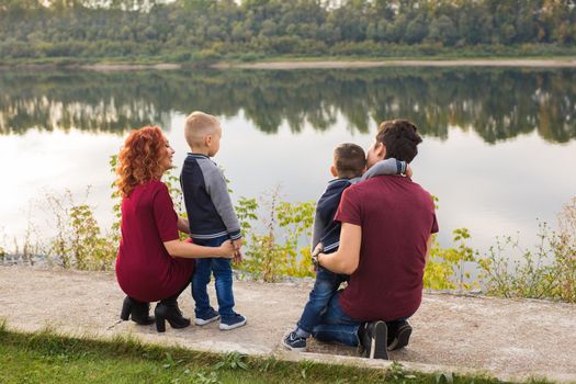 Parenthood, childhood and family concept - Parents and two male children walking at the park and looking on something.