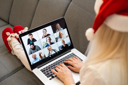 A young smiling woman wearing red Santa Claus hat making video call on social network with family and friends on Christmas day.