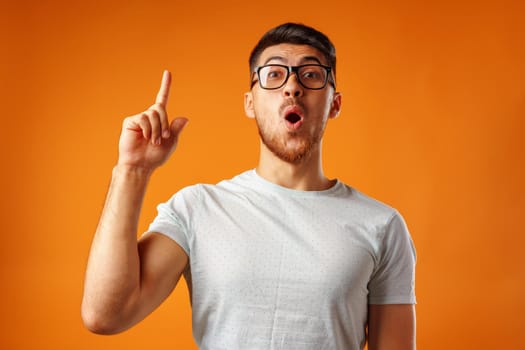 Nerdy surprised man in glasses who has an idea putting his finger up against yellow background