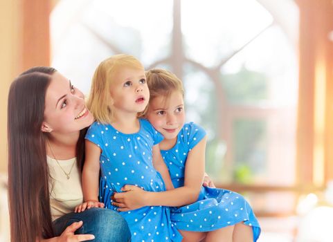 The concept of family happiness and mutual understanding between parents and children.Beautiful young mother with her two daughters. On the background of the hall with large semi-circular window.
