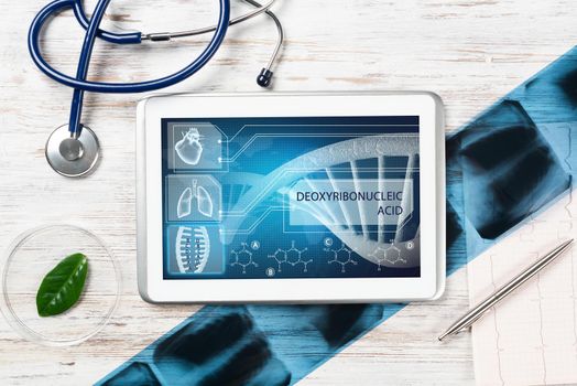 Human genetic research in medical laboratory. Tablet computer with DNA helix structure on screen. Stethoscope, x-ray image and cardiogram on wooden desk. Medical diagnostics and patient genome testing