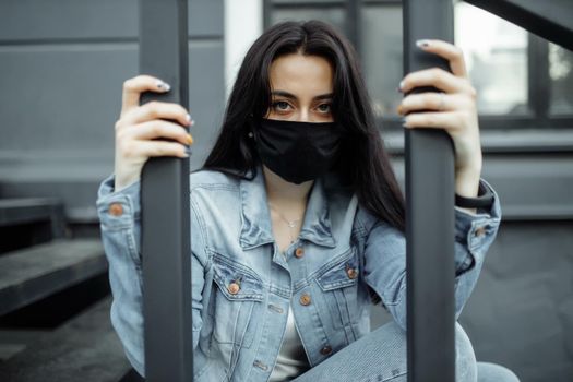 Sad teenager girl in medical mask behind bars. Schools are quarantined due to illness, epidemics. Coronavirus pandemic. Covid 19.