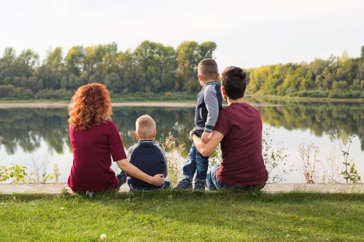 Childhood and nature concept - Family with little sons sitting on the green grass.