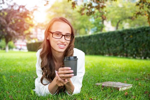 portrait of a young attractive woman in the park with a paper glass of coffee. Rest in the park