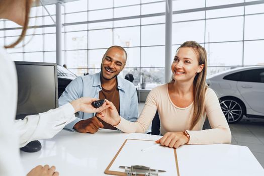 Beautiful young couple signs documents at car dealership showroom sitting at the table