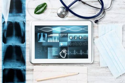 Medical diagnostics in modern hospital. Tablet computer with medical application interface on screen. Top view x-ray images, stethoscope and cardiogram on wooden desk. Digital technology in clinic.