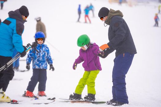 Instructors teach a child on a snow slope to snowboard