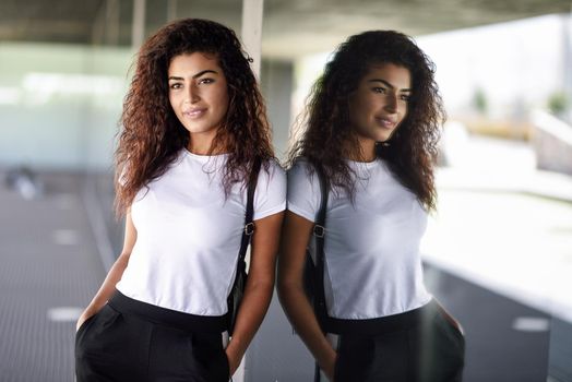 Young African woman with black curly hairstyle standing near business building. Happy Arab girl in sport clothes in the street.