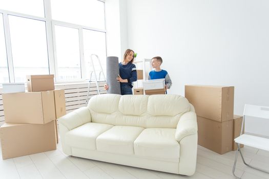 Young cute single mother and son are happy about the move to new house holding a pot of greens and carpet in their hands. Concept of housewarming and family space extensions