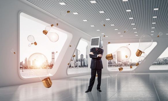 Businessman in suit with monitor instead of head keeping arms crossed while standing among flying and glowing lightbulbs inside office building. 3D rendering.