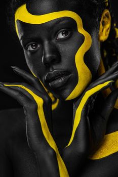 Face art. Woman with black and yellow body paint. Young african girl with colorful bodypaint. An amazing afro american model with yellow makeup.