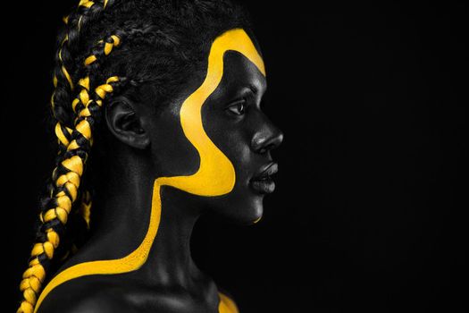 Face art. Woman with black and yellow body paint. Young african girl with colorful bodypaint. An amazing afro american model with yellow makeup.