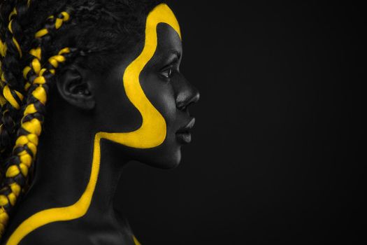 Face art. Woman with black and yellow body paint. Young african girl with colorful bodypaint. An amazing afro american model with yellow makeup.