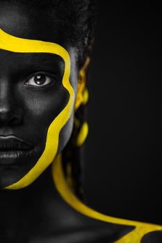 Face art. Woman with black and yellow body paint. Young african girl with colorful bodypaint. An amazing afro american model with yellow makeup.