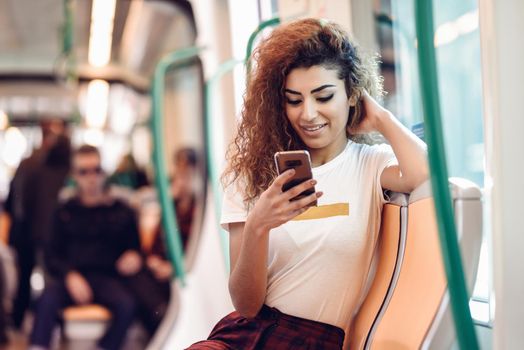 Arabic woman inside subway train looking at her smart phone. Arab girl in casual clothes.