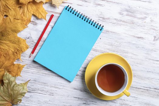 Flat lay autumn composition with cup of black tea and yellow autumn leaves. Time of tea break concept. Still life of hot drink and notepad with pen lies on vintage wooden desk with bright foliage.