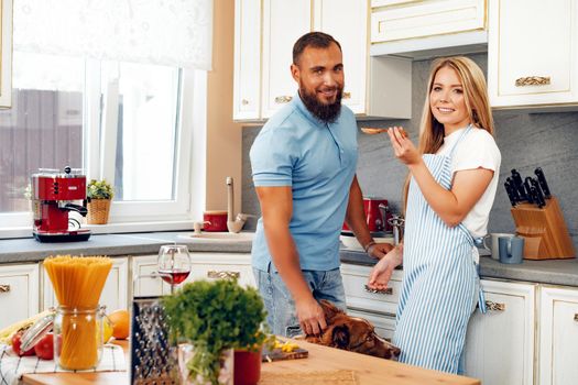 Happy smiling couple cooking food at kitchen with their dog