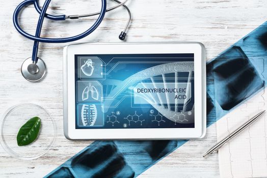 Human genetic research in medical laboratory. Tablet computer with DNA helix structure on screen. Stethoscope, x-ray image and cardiogram on wooden desk. Medical diagnostics and patient genome testing