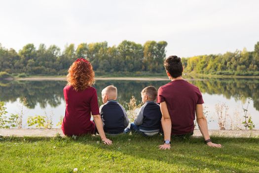 Childhood and nature concept - Family with little sons sitting on the green grass.