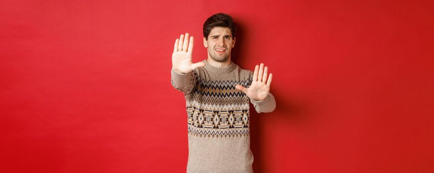 Image of disappointed handsome man, asking to stop, rejecting something awful, standing displeased against red background.