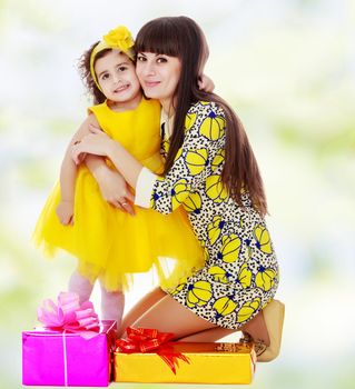 Beautiful young mother and her cute little daughter , embracing, surrounded by Christmas gifts.white-green blurred abstract background with snowflakes.