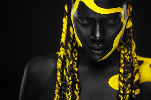 Face art. Woman with black and yellow body paint. Young african girl with colorful bodypaint. An amazing afro american model with yellow makeup.