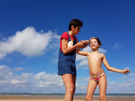 Mother throwing sunscreen on her little daughter on a tropical beach