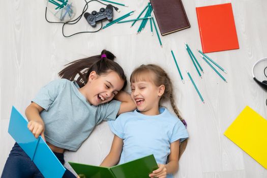 two little girls sisters reading a book lying on the floor