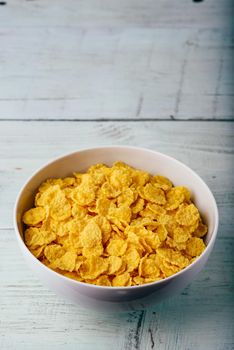 White bowl of corn flakes on a wooden surface