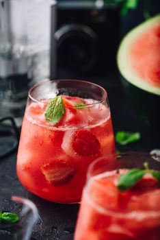 Fresh watermelon and strawberry cocktail with mint garnish on dark concrete background