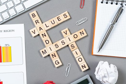 Brand value concept with words from cubes. Still life of office workplace with crossword. Flat lay grey surface with notebook and infographics. Strategy planning and business management.