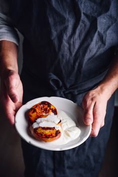 Plate with baked peaches with honey and whipped cream in chefs hands