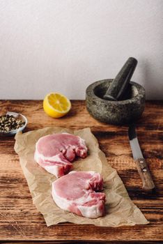 Two pork loin steaks on baking paper with lemon and peppercorn